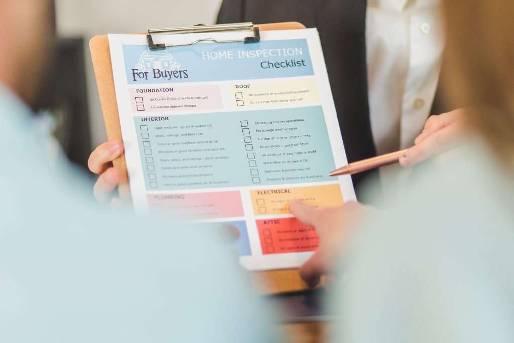 Real estate inspector and home buyers reviewing a colorful printed home inspection checklist on a wooden clipboard