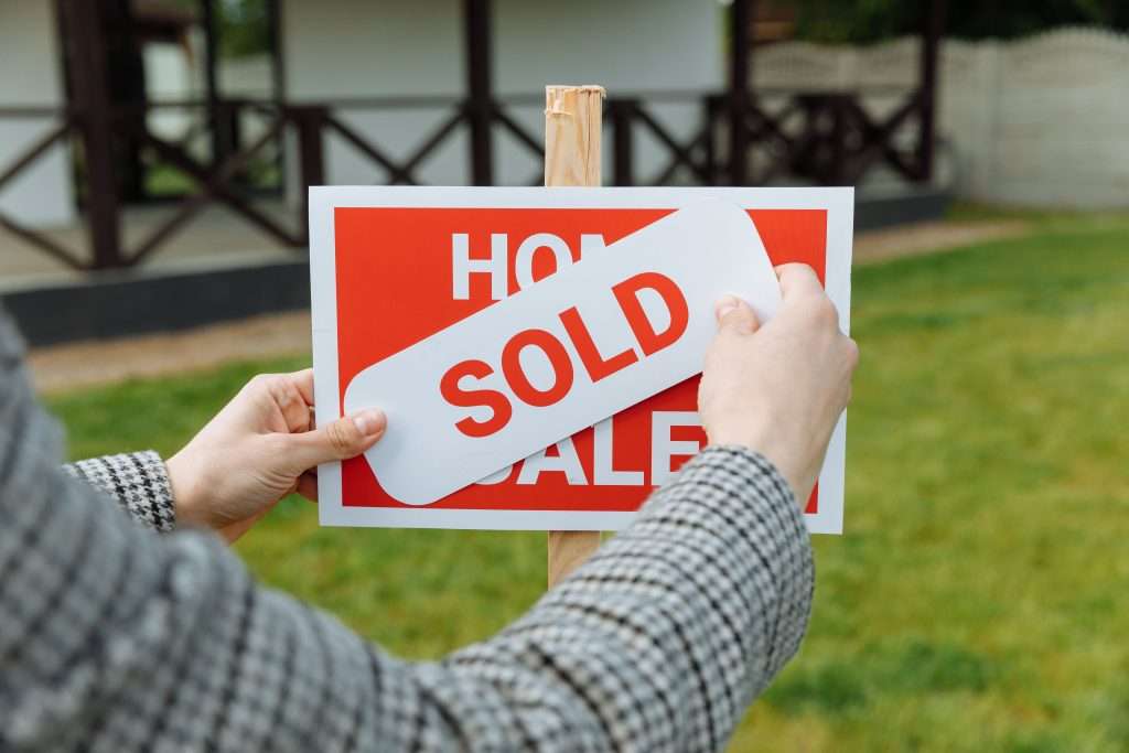 Real estate agent placing a white "SOLD" sticker across a red "FOR SALE" yard sign