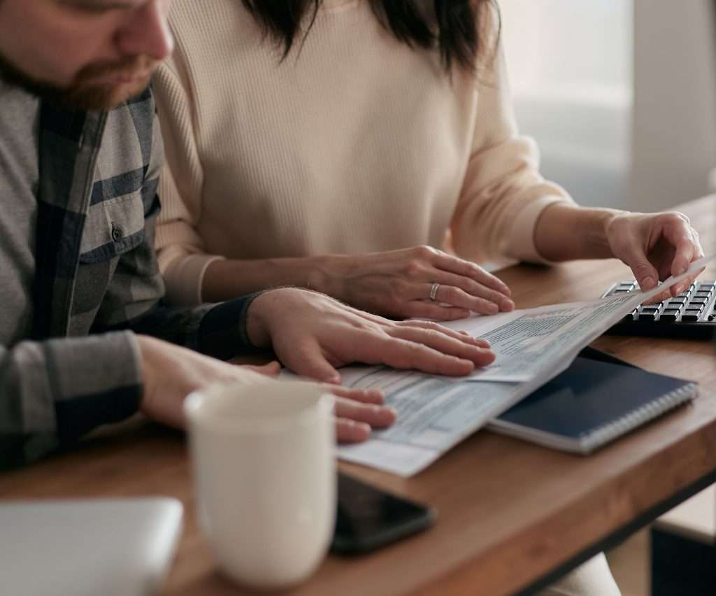 Couple sitting at a table carefully reviewing bills and property tax documents together next to a calculator and coffee cup